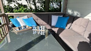 Un espace extérieur lumineux, aménagé pour se détendre, avec une table en verre, des coussins et un plateau rempli de boissons.