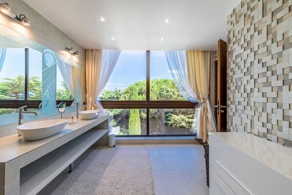 Un baño moderno con un ventanal grande, un lavamanos blanco y una alfombra color crema.