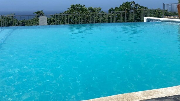 A clear blue pool with a view of the ocean and a metal fence. - Amore Villa Retreat in Ocho Rios (Ocho Rios)