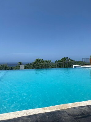 En klar, blå pool med udsigt over havet og et metalhegn.