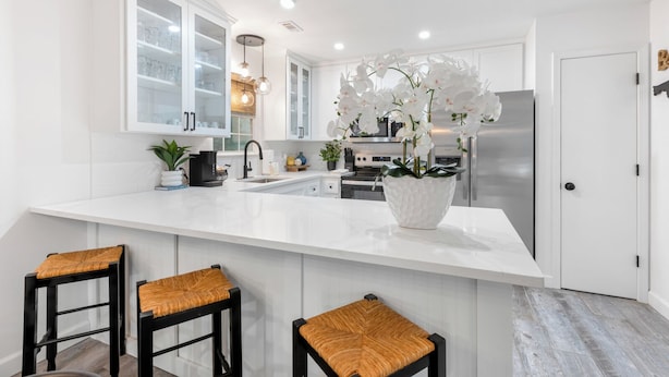 Una cocina moderna con armarios blancos, una isla grande con taburetes de bar y una orquídea en maceta como centro de mesa.