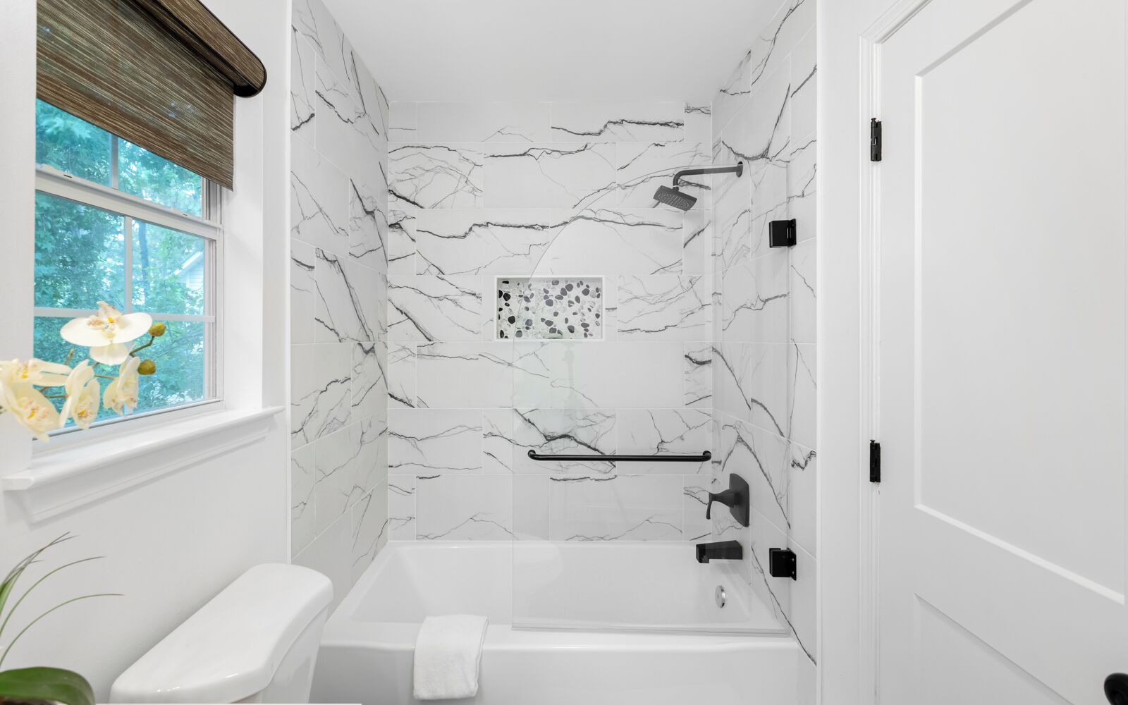 Un baño con bañera, ventana con vistas a árboles y pared de mármol.