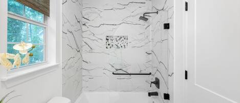 Un baño con bañera, ventana con vistas a árboles y pared de mármol.