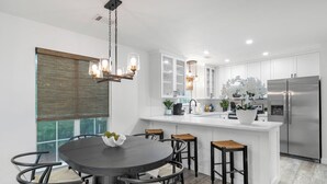 Una cocina moderna con armarios blancos, un refrigerador de acero inoxidable, una mesa redonda de comedor con taburetes de bar y una araña.