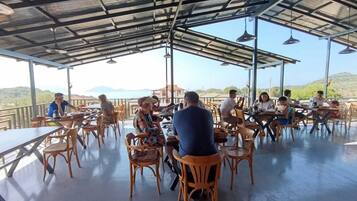 Un área de comedor al aire libre con mesas y sillas, un techo de metal y vistas al paisaje.