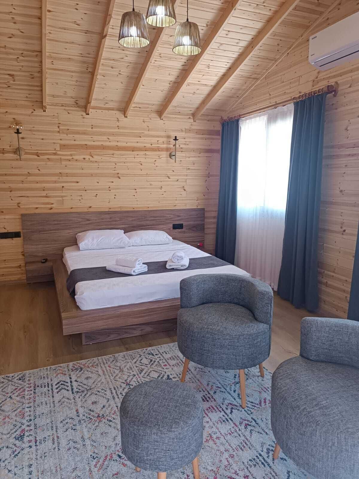 A wooden-paneled bedroom with a bed, two grey armchairs, and a patterned rug.