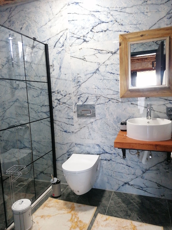 A bathroom with a glass shower enclosure, a white toilet, a sink with a wooden countertop, and a mirror above the sink. - Habesa Bungalov & Apart (Kas)