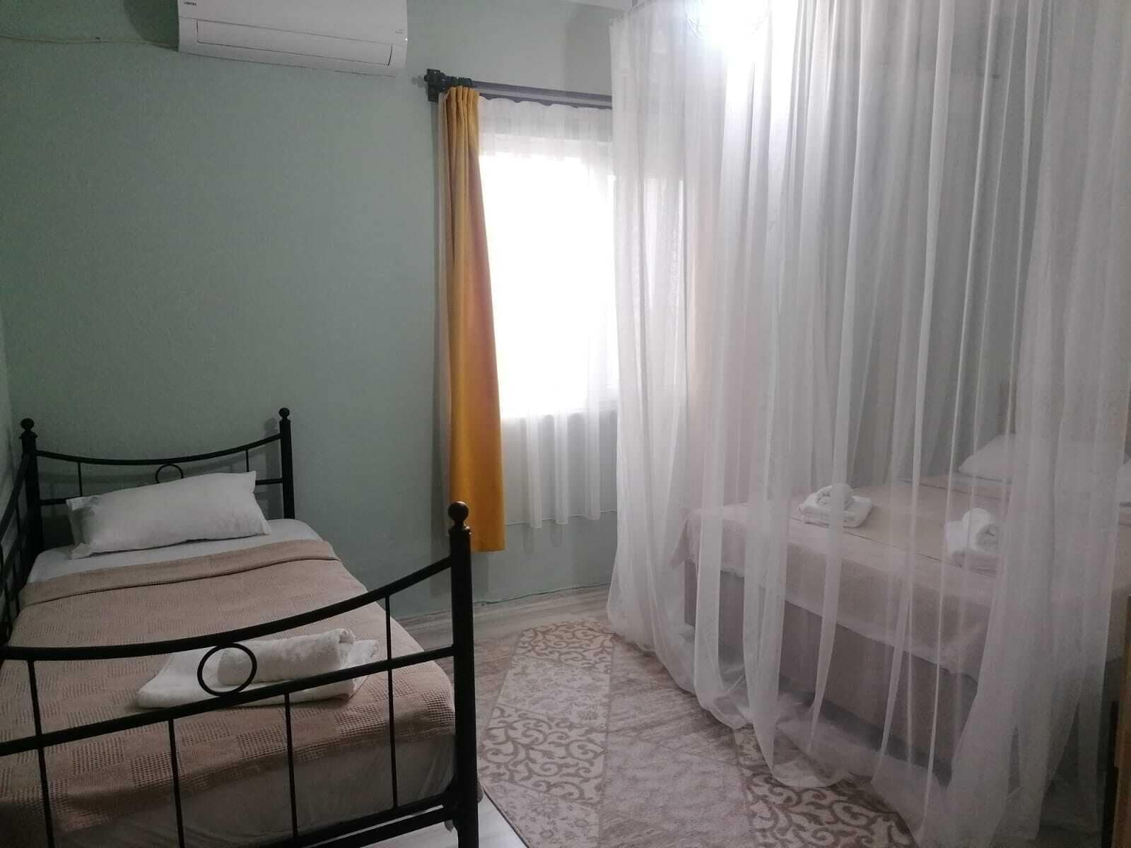 A bedroom with a bed, a bedside table, a chair, and a window with sheer curtains.