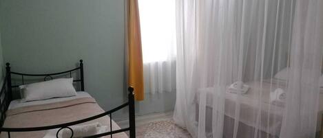 A bedroom with a bed, a bedside table, a chair, and a window with sheer curtains.