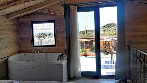 A wooden cabin with a large bathtub, a window with a view of the outside, and a balcony with a railing. - Habesa Bungalov & Apart (Kas)