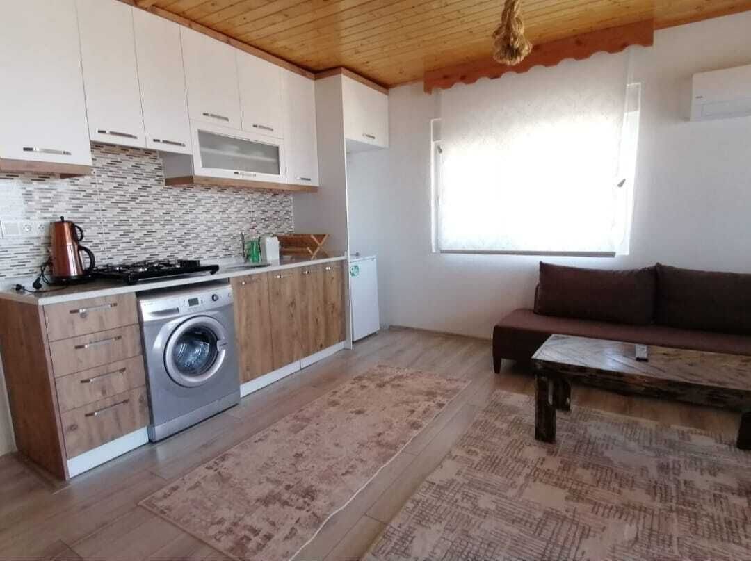 A compact kitchen with a washing machine, wooden cabinets, and a large window.