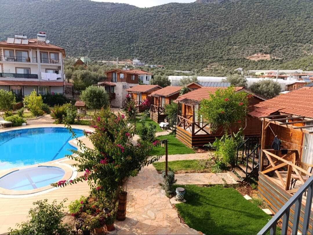 Un resort con piscina, cabañas de madera y montañas al fondo.
