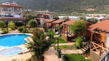 Un resort con piscina, cabañas de madera y montañas al fondo.