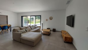 A spacious living room with a large sectional sofa, a wooden coffee table, and a flat-screen TV mounted on the wall. - Villa Venturon Proche la Plage de Pinarello Avec Piscine et Cuisine D'été (Zonza)