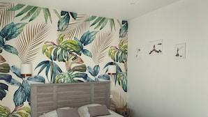 A bedroom with a bed, two bedside lamps, a wall with tropical leaf wallpaper, and a small bedside table with a lamp. - Villa Venturon Proche la Plage de Pinarello Avec Piscine et Cuisine D'été (Zonza)