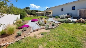 A well-maintained garden with a gravel path, various plants, and a white building with a tiled roof. - Villa Venturon Proche la Plage de Pinarello Avec Piscine et Cuisine D'été (Zonza)