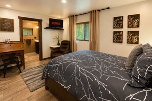 Une chambre à coucher avec un lit, un bureau, une chaise, une télévision et des œuvres d’art accrochées aux murs.