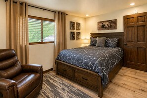 A bedroom with a bed, a chair, a wooden wardrobe, and a window with curtains.