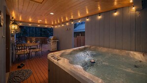 Ein Whirlpool auf einer Holzterrasse mit Lichterketten, einem Grill und einem Tisch mit Stühlen.