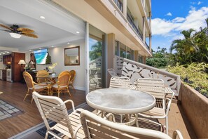 Une chambre d’hôtel moderne avec balcon, un coin repas doté de meubles en osier et un grand écran de télévision.