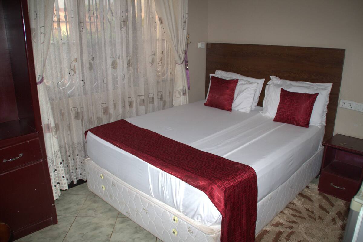 A neatly made bed with a wooden headboard, a red throw blanket, and two red pillows.