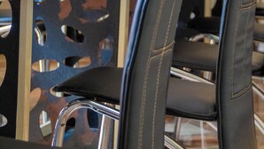 Une chambre d’hôtel avec une table en verre, des fauteuils en cuir noir et un rideau orné d’un motif circulaire.