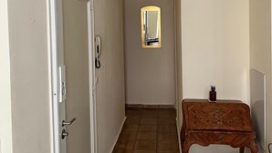 Un passadís amb una porta a l'esquerra, una taula petita amb un mirall a la dreta i una cadira al davant de la taula.