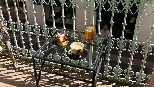 Un balcó amb una taula de vidre, una tassa de cafè i un pastís.
