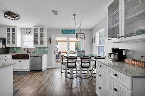 Una cocina con armarios blancos, lavavajillas, cafetera y un letrero que dice 'BEACH HOUSE'.