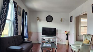 Un salon avec un canapé, un téléviseur posé sur un meuble, une table basse avec des livres, un vase rempli de fleurs et un fauteuil.