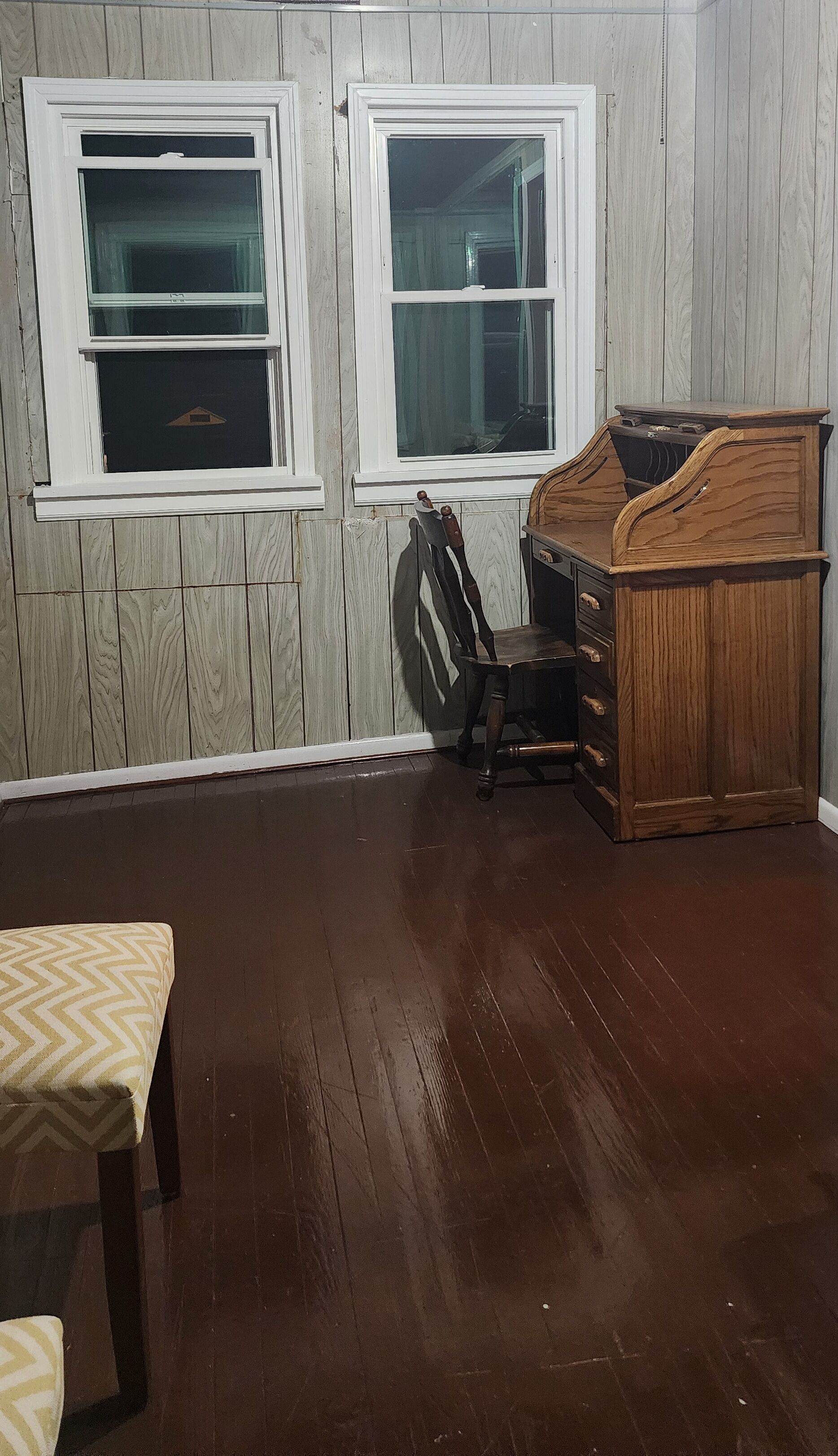 A room with two windows, a wooden dresser, a chair, and a table with a patterned tablecloth.