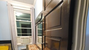 Une petite pièce comprenant un lit, un radiateur, une fenêtre avec des rideaux et une armoire.