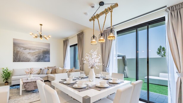A modern dining area with a white table set for six, surrounded by white chairs.