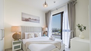 A modern hotel room with a large bed, bedside lamps, a view of the city, and a plant on the desk.