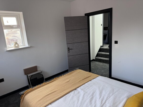 Un dormitorio con cama, armario, una mesita y ventana.