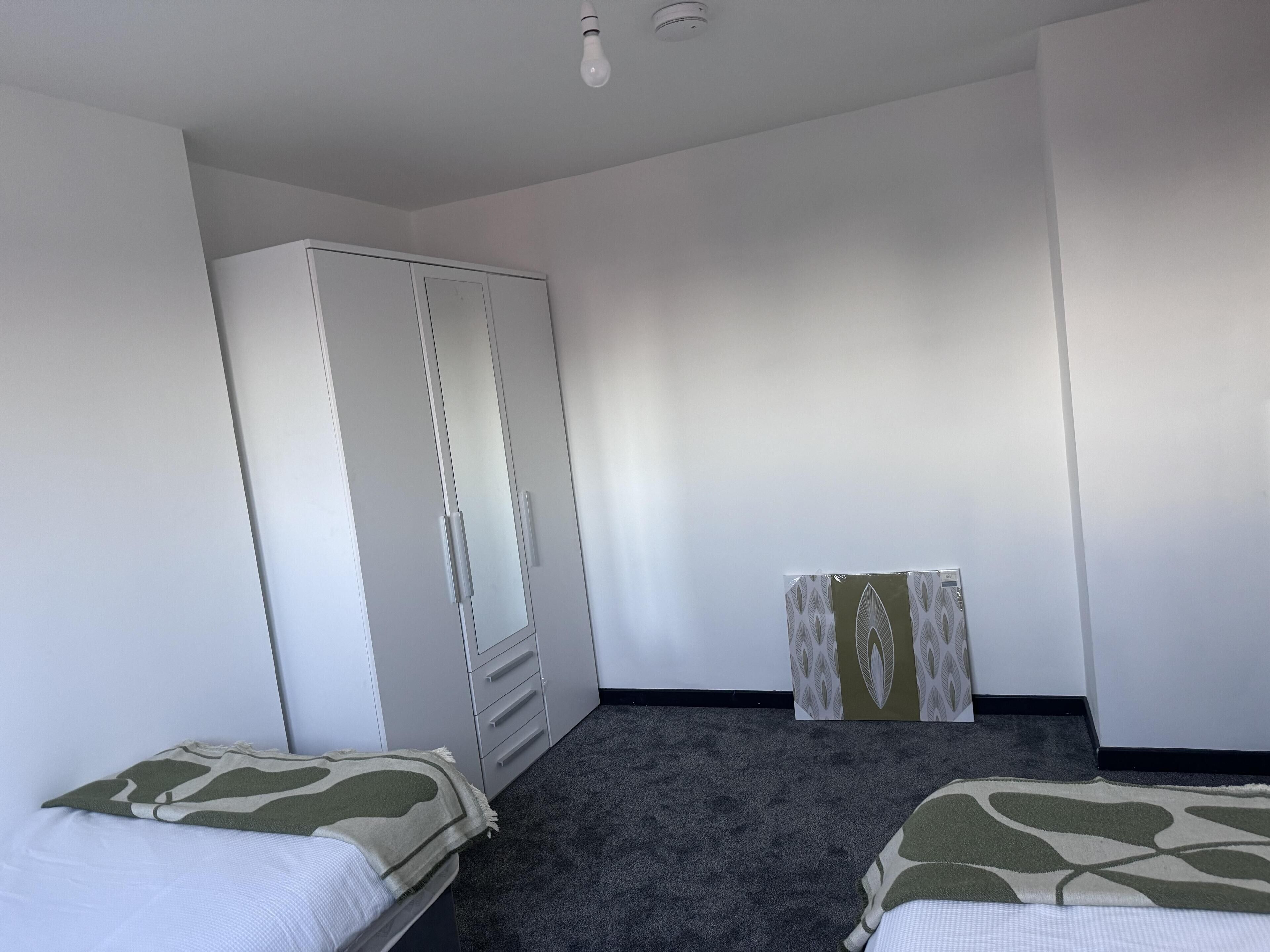 Une chambre avec deux lits, une armoire et une petite table recouverte d’une nappe à motifs.