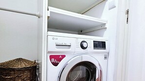 Een compacte witte wasmachine met bedieningspaneel, een wasmand en een betegelde vloer.