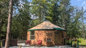 A small, single-story cabin with a green roof, surrounded by trees. There is a picnic table in the foreground and a grill outside the cabin. - Romantic Hot Tub Get-a-way! (Coleraine)
