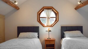 A bedroom with two beds, a window with curtains, a bedside table with a lamp, and wooden beams on the ceiling. - Forge Masters Cottage (Middlewich)