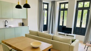 A modern kitchen with a dining area, a sofa, and large windows with curtains. - Sueño Indiano, Bajo Norte (Muros de Nalón)