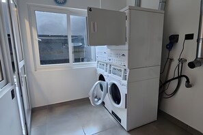 A compact laundry area with a washing machine and dryer, a window, and a wall-mounted electrical outlet.