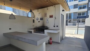 Zona cuina exterior amb taulell de formigó, una barbacoa i un extintor.