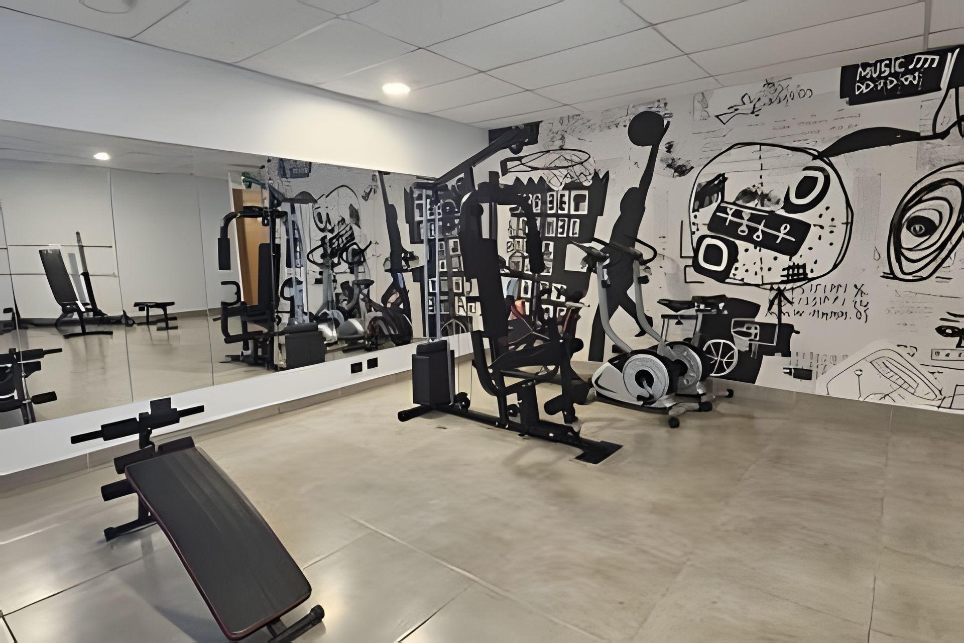 Ein Fitnessstudio mit unterschiedlichen Trainingsgeräten, einem großen Spiegel und einer Wand mit abstrakten Graffiti-Kunstwerken.