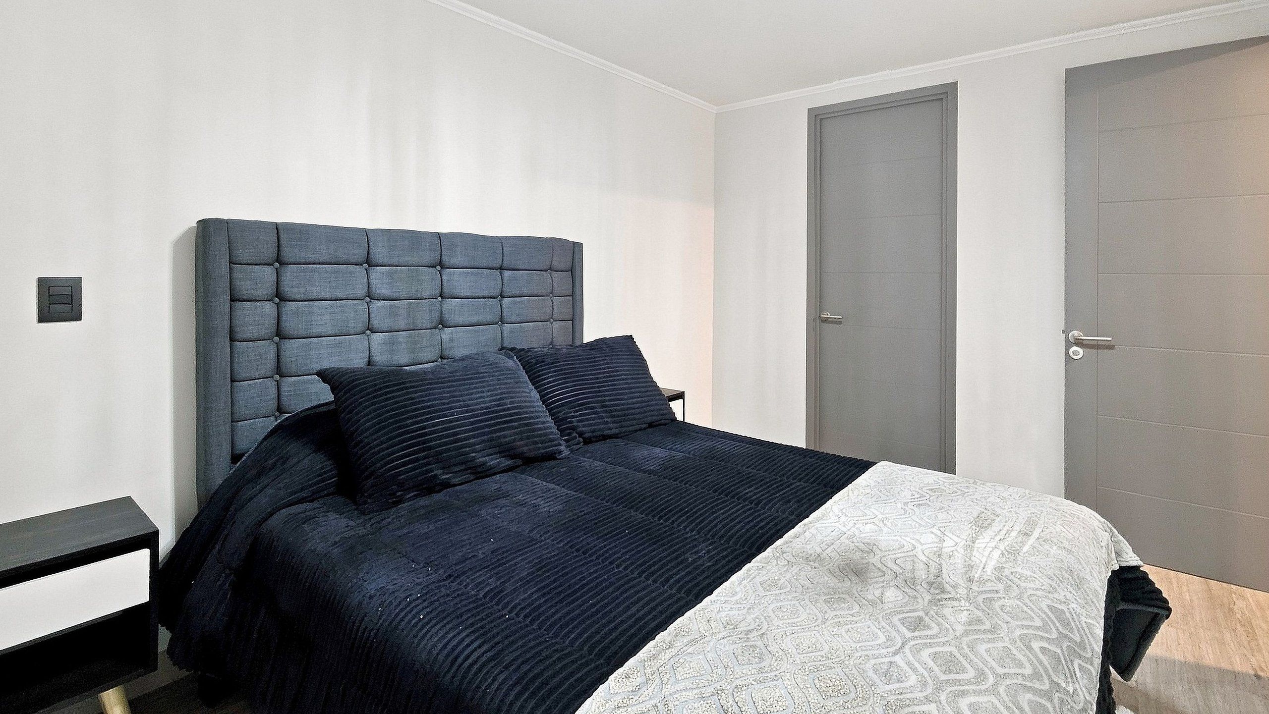A bedroom with a bed, a nightstand, a door, and a wall switch.