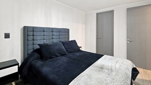 A bedroom with a bed, a nightstand, a door, and a wall switch. -  Oceana Suites Briones Luco (Santiago)