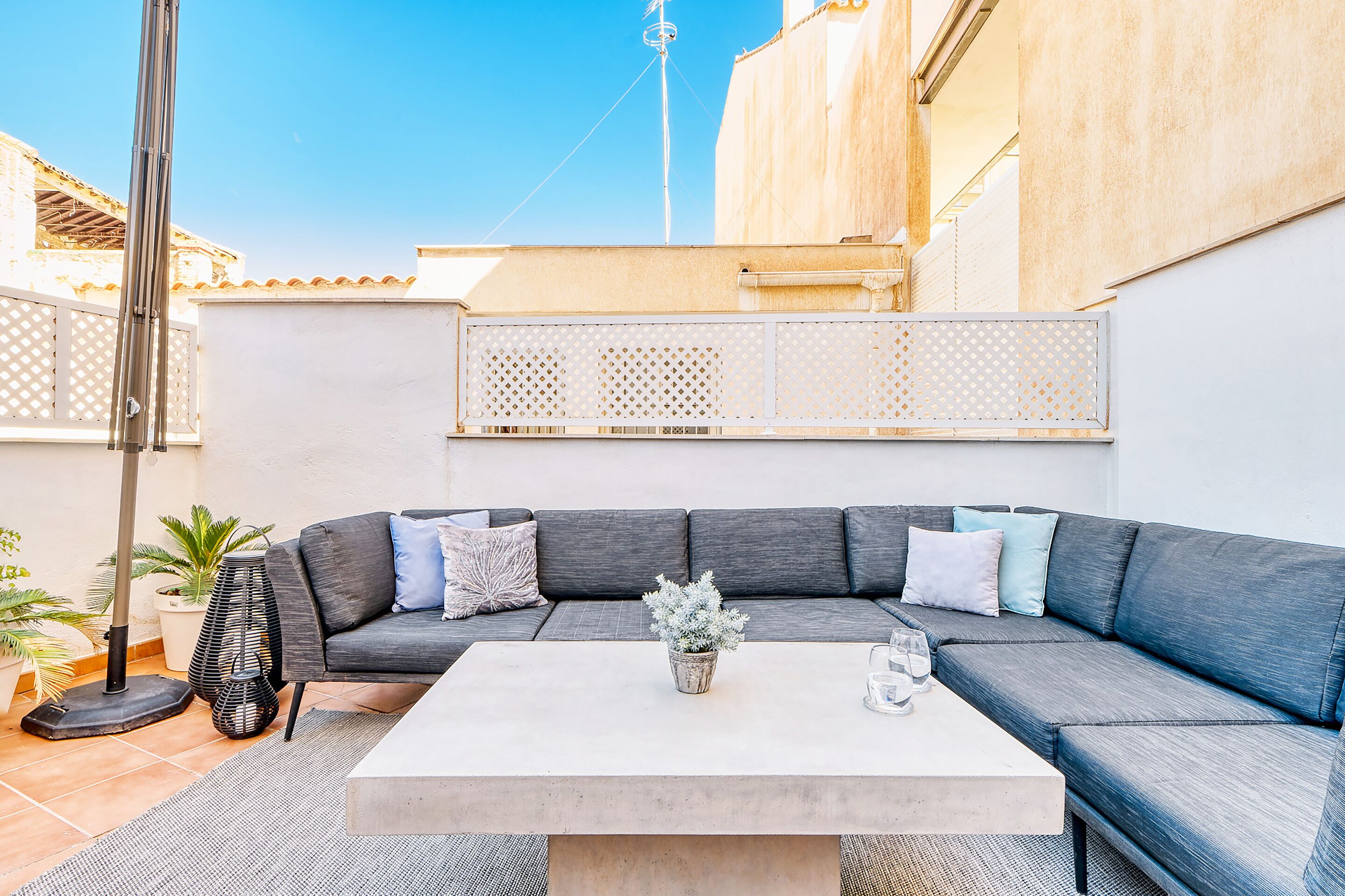 A modern outdoor living area with a grey sectional sofa, a white coffee table, and a potted plant.