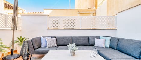 A modern outdoor living area with a grey sectional sofa, a white coffee table, and a potted plant.
