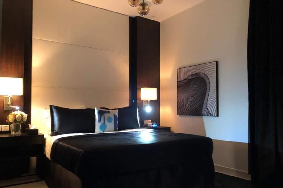 A hotel room with a large bed, bedside lamps, a nightstand with a vase of flowers, and a wall-mounted artwork.