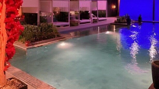 A nighttime view of a swimming pool with a clear water surface, surrounded by a low wall and a few lounge chairs. - Dana Serviced Apartments2 (Riyadh)