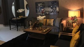 A modern living room with a sofa, coffee table, and a painting of a cityscape. - Dana Serviced Apartments2 (Riyadh)